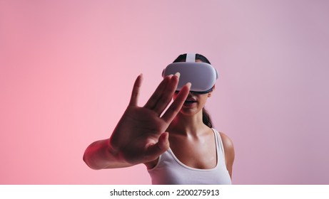 Female gamer using her hand to interact with virtual space while wearing a virtual reality headset. Young woman experiencing a 3D simulation in a studio. - Powered by Shutterstock