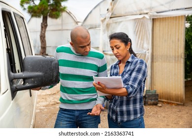 Female Gardener Discussing Contract For Transportation Of Agricultural Products With Representative Of Transport Company Outdoors Against Background Of Greenhouses