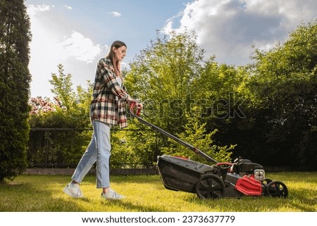 Female gardener working in autumn, cutting grass in backyard. Concept of gardening, work, nature. Housework, gardening and country life. Home garden grass cutting woman mowing with lawn mower. Stockfoto © 