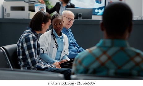 Female General Practitioner Consulting Asian Patient In Waiting Area Lobby To Give Sickness Diagnosis And Healthcare Treatment. Doctor Giving Support To Ill Person At Hospital Reception.