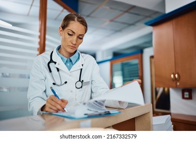 Female General Practitioner Filling Medical Records While Working In The Hospital.