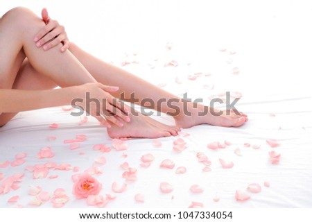 female gentle legs and hands caressing them setting on white surface with rose petals.
