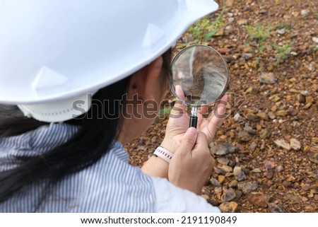 Female geologist using a magnifying glass examines nature, analyzing rocks or pebbles. Researchers collect samples of biological materials. Environmental and ecology research.