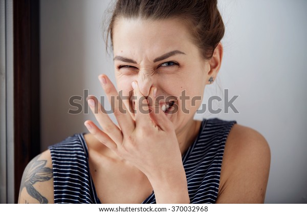 Female gesture smells\
bad. Headshot woman pinches nose with fingers hands looks with\
disgust something stinks bad smell situation. Human face expression\
body language reaction