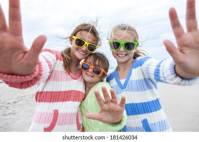 Female Girl Children Having Fun Wearing Sunglasses & Waving To A Camera Taking Selfie Photograph On A Beach