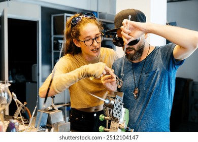 A female glassblowing teacher instructs a student in a workshop. She is explaining a technique while the student watches intently and performs it. - Powered by Shutterstock