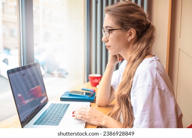 Female in glasses successful business analyst reading newsletter on laptop computer while sitting in coffee shop during recreation time. Woman content writer checking e-mail on notebook gadget  - Powered by Shutterstock