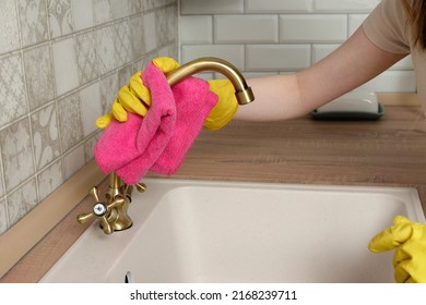 Female in gloves wipes faucet with rag.  Woman cleans kitchen