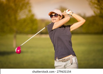 Female Golf Player Swinging Driver Club From Tee Box At Twilight.