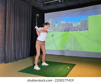 Female golfer plays golf on golf simulator. Indoor golf - Shutterstock ID 2250177419