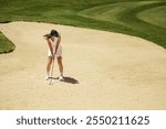 Female golfer in sand bunker aiming and preparing to take a shot. She maintains a focused stance as she concentrates on striking the golf ball.