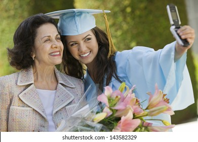 Female graduate and grandmother taking picture with cellphone outside