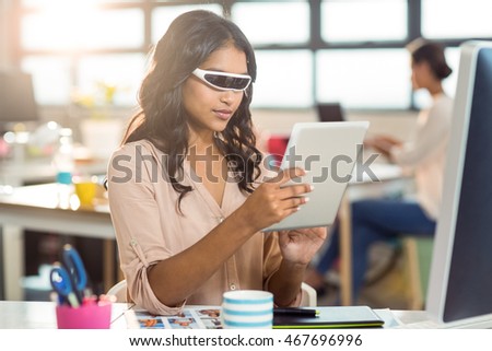 Female graphic designer in virtual reality video glass using digital tablet in office