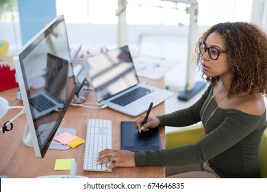 Female Graphic Designer Working On Computer While Using Graphic Tablet At Desk In The Office