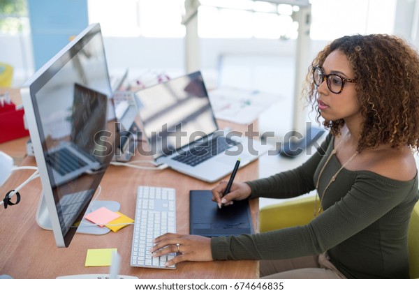 Female graphic designer working on\
computer while using graphic tablet at desk in the\
office