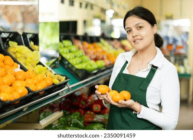 Female grocery store worker lays out ripe tangerines on the counter and display case