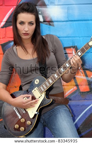 female guitar player in front of a tagged wall