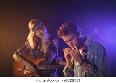 Female guitarist looking at male musician playing harmonica in music concert - Powered by Shutterstock