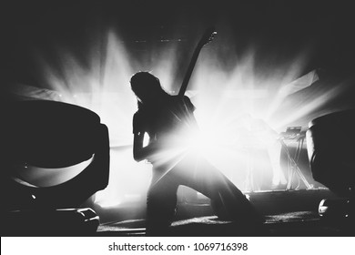 Female guitarist silhouette playing guitar solo on a stage on a knees 