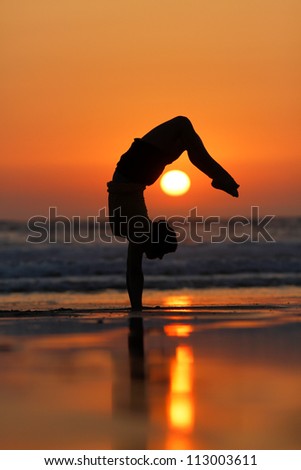 female gymnast doing a handstand in sunset at beach
