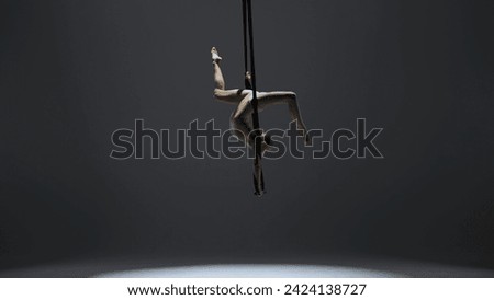 Female gymnast isolated on monochrome studio background. Girl aerial dancer on acrobatic trapeze with straps spinning in split.