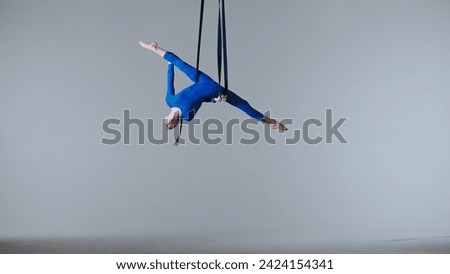 Female gymnast isolated on white studio background. Girl aerial dancer balancing spinning on gymnastic straps, showing dance elements