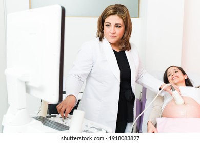 Female gynecologist in her 40s using an ultrasound machine in her office. Happy pregnant woman looking at the sonogram of her baby in the screen
