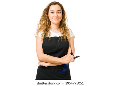 Female Hair Stylist Working And Cutting Hair At The Beauty Salon. Beautiful Young Woman With A Black Apron While Holding A Brush And Scissors