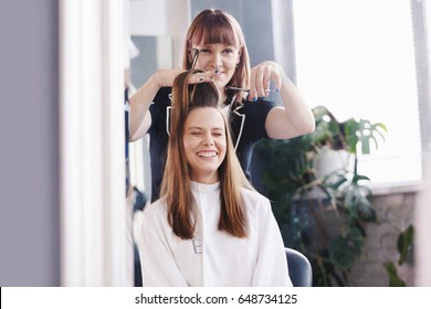 Female Hairdresser With Comb And Scissors Makes A Haircut For A Woman Closeup In Beauty Salon