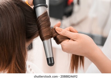 Female Hairdresser Curling Hair Of Client In Beauty Salon, Closeup