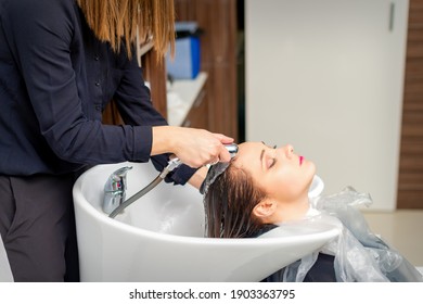 A Female Hairdresser Is Rinsing The Hair Of A Young Woman In A Sink After Shampooing In A Hair Salon