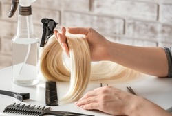 Female Hairdresser With Strand Of Blonde Hair At Table In Beauty Salon