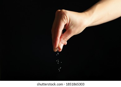 Female hand adding salt on black background