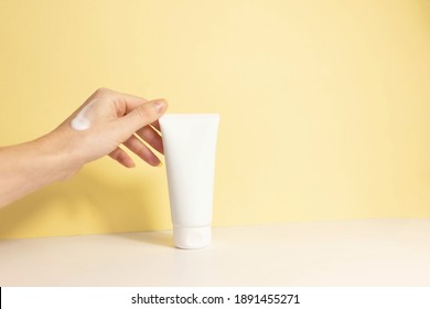 
Female Hand With Applied Cream Touches Cosmetic Tube On Beige Background. Concept Of Cream, Hand Lotion. Winter Skin Care. Copy Space