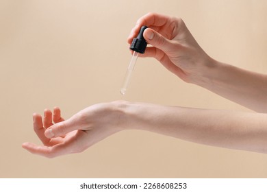 Female hand applying serum from pipette to her wrist on beige isolated background. Concept of cosmetic products for skin care, beauty and spa. - Powered by Shutterstock