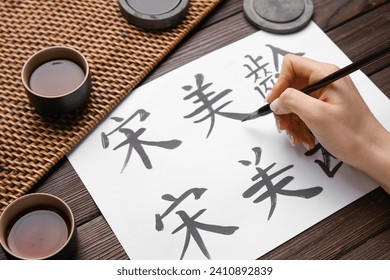 Female hand with Asian hieroglyphs, brush and cups of tea on wooden background, closeup. International Haiku Poetry Day - Powered by Shutterstock