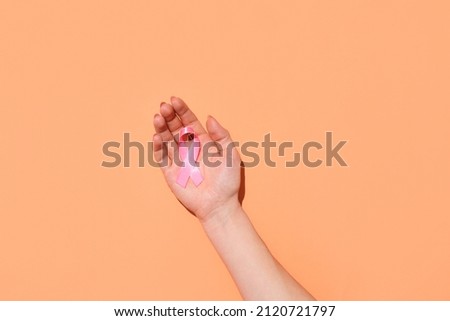 Female hand with awareness ribbon on color background. World Cancer Day