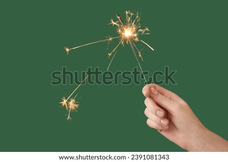 Female hand with beautiful Christmas sparkler on green background