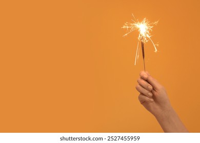 Female hand with beautiful Christmas sparklers on orange background - Powered by Shutterstock