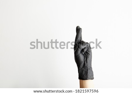 Female hand in black latex gloves crossing fingers for hope, isolated on white background with free space for text