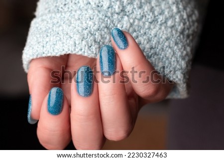 Female hand in blue knitted sweater with beautiful manicure - blue glitter nails. Nail care concept