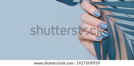Female hand with blue nail design. Blue nail polish manicure. Female hand hold tropic plant leaf. Blue nail art decoration. Copy space.