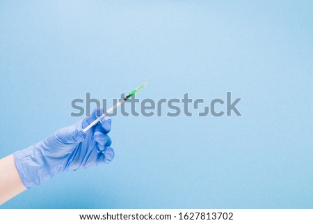 female hand in a blue rubber medical glove holds an insulin syringe with green colored medicine, the vaccine inside on a blue background copy space, treatment and health care concept, diabetes concept