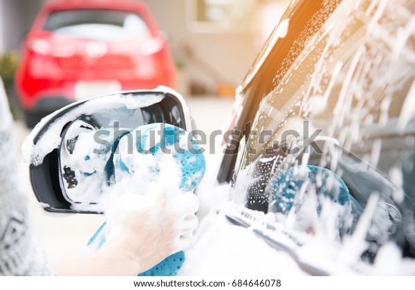 Female hand with blue sponge clean washing car side\
mirror. concept car\
wash.