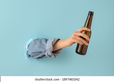 Female hand with bottle of beer breaks through blue paper background. - Powered by Shutterstock