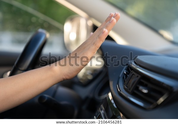 Female hand checking air conditioning panel\
inside car. Woman driver suffer from heat in vehicle holding hand\
at conditioning system cooling grid. Hot summer season and driving\
automobile concept
