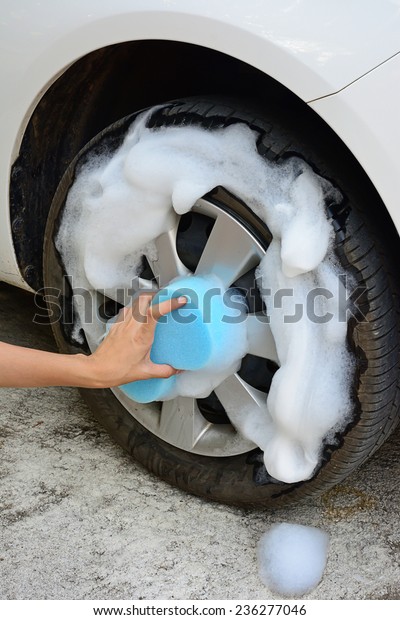 female hand is cleaning car tire with blue sponge;\
selective focus at hand