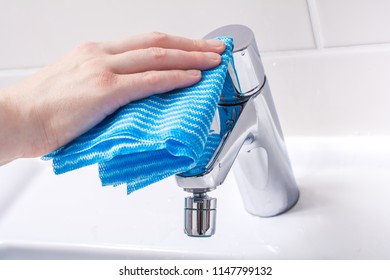 Female Hand Cleaning The Handle Of A Chrome Faucet With A Towel In Bathroom