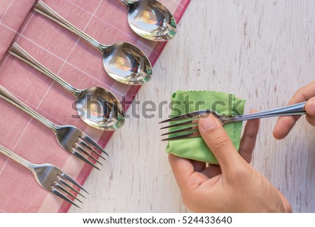 Female hand cleaning spotty silverware with a cleaning product and a cloth,Close up woman hand cleaning silver spoon,polished silver,