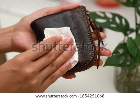 Female hand cleaning the surface of the leather wallet. Coronavirus prevention, hygiene to stop spreading coronavirus.